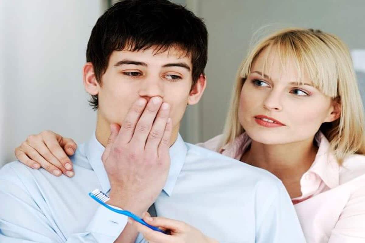 man covering mouth with woman offering him a toothbrush