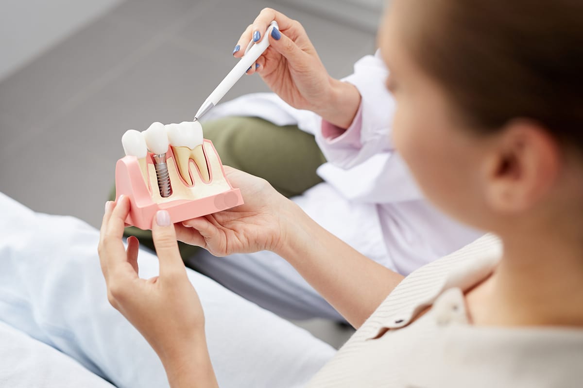 woman looking at a model of a single tooth dental implant