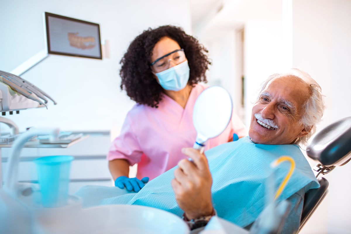 older man in dentist chair examining his smile in mirror